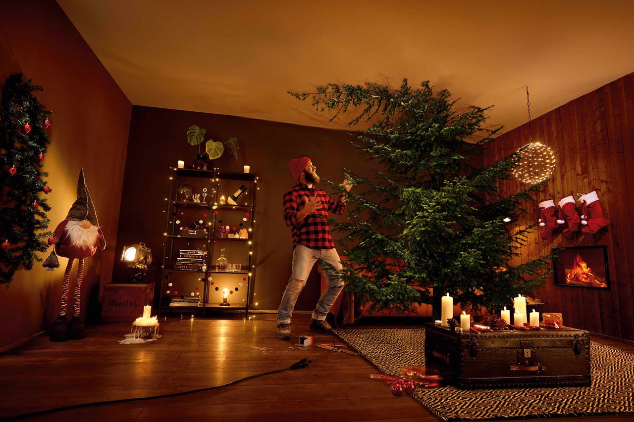 Vardagsrum med dekorerad julgran och man som sätter upp julgransdekorationer