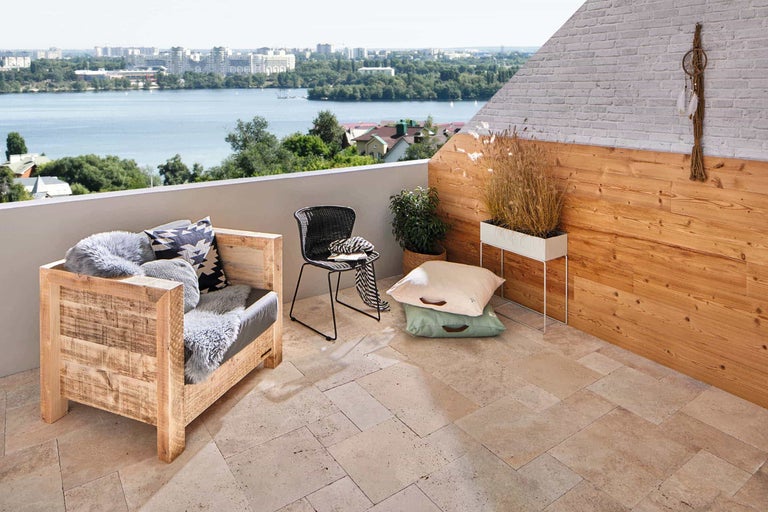 Balkong med trämöbler, stol, kuddar och utsikt över en sjö