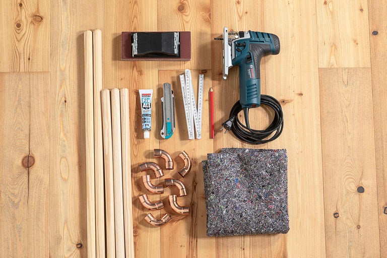 Arbetsbänk med sticksåg, träpinnar, slipkloss, lim, skärare, tumstock, penna, kopparrör och fleece