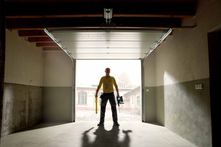 Öppen garageport med en man som håller verktyg