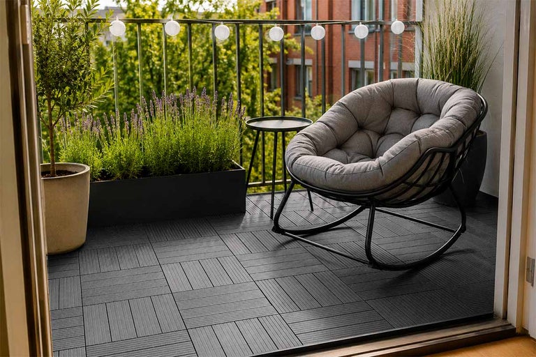 Modern balkong med mörkgrå trallplattor, grå gungstol med dyna, sidobord, lavendel i en blomlåda och ljusslinga på räcket.