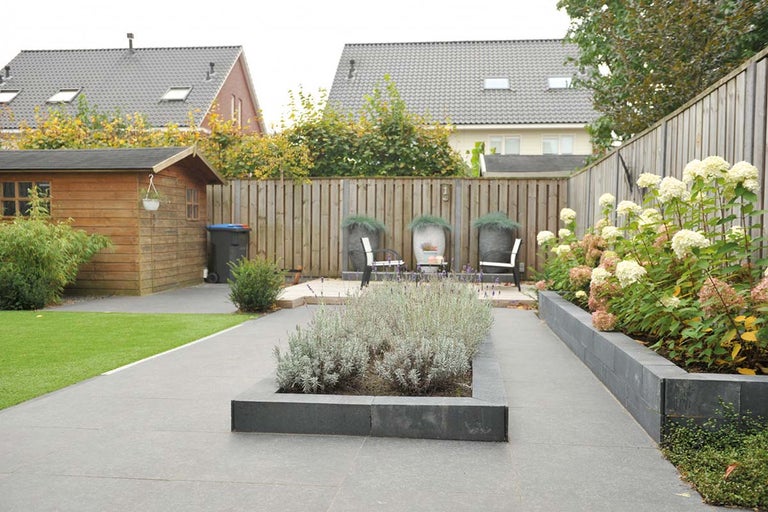 En trädgård med trädgårdshus, gräsmatta, stenläggning och planteringar