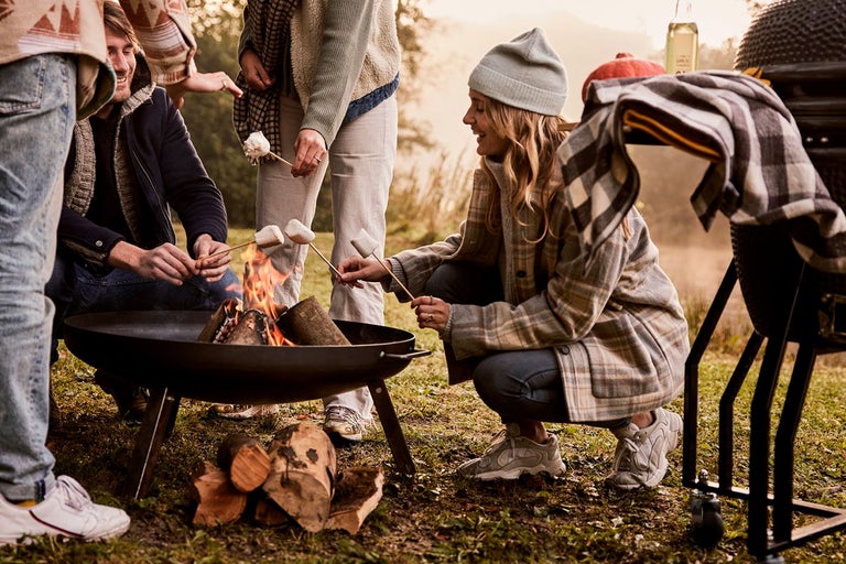 Grupp av människor som rostar marshmallows över en eldfat utomhus.