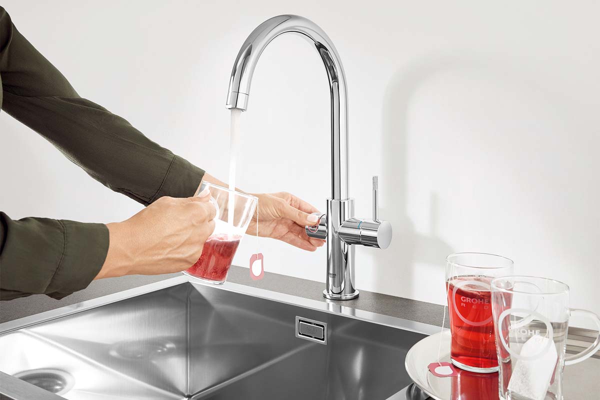 Person fyller glas med vatten under kromad köksblandare