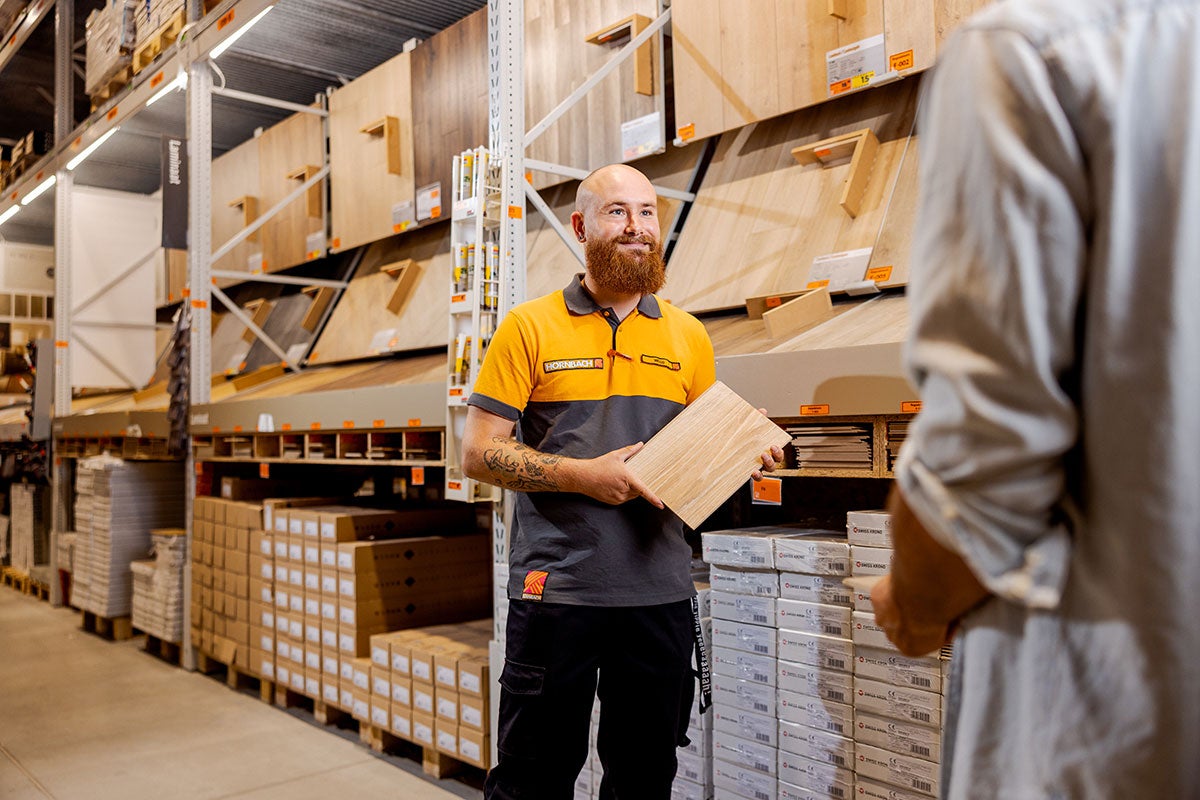 En Hornbach-anställd håller ett laminatprov i handen, med en hylla med laminat i bakgrunden.