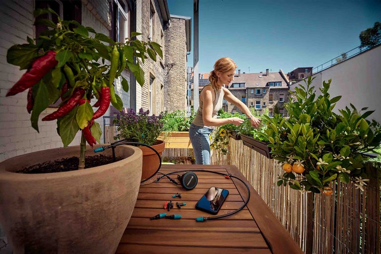 En kvinna installerar ett Gardena Micro-Drip-System för automatisk bevattning av balkongväxter som paprika, örter och citrusträd.