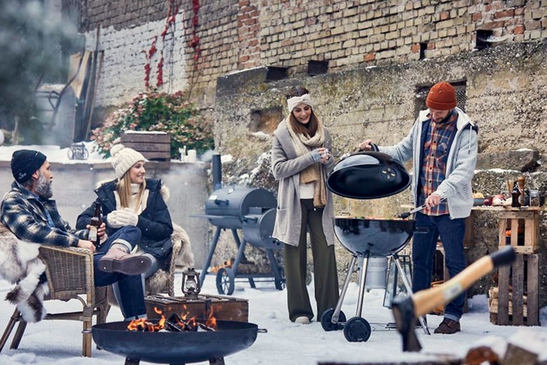 Grillscen på vintern med kolgrill, eldstad och flera personer utomhus framför en tegelvägg