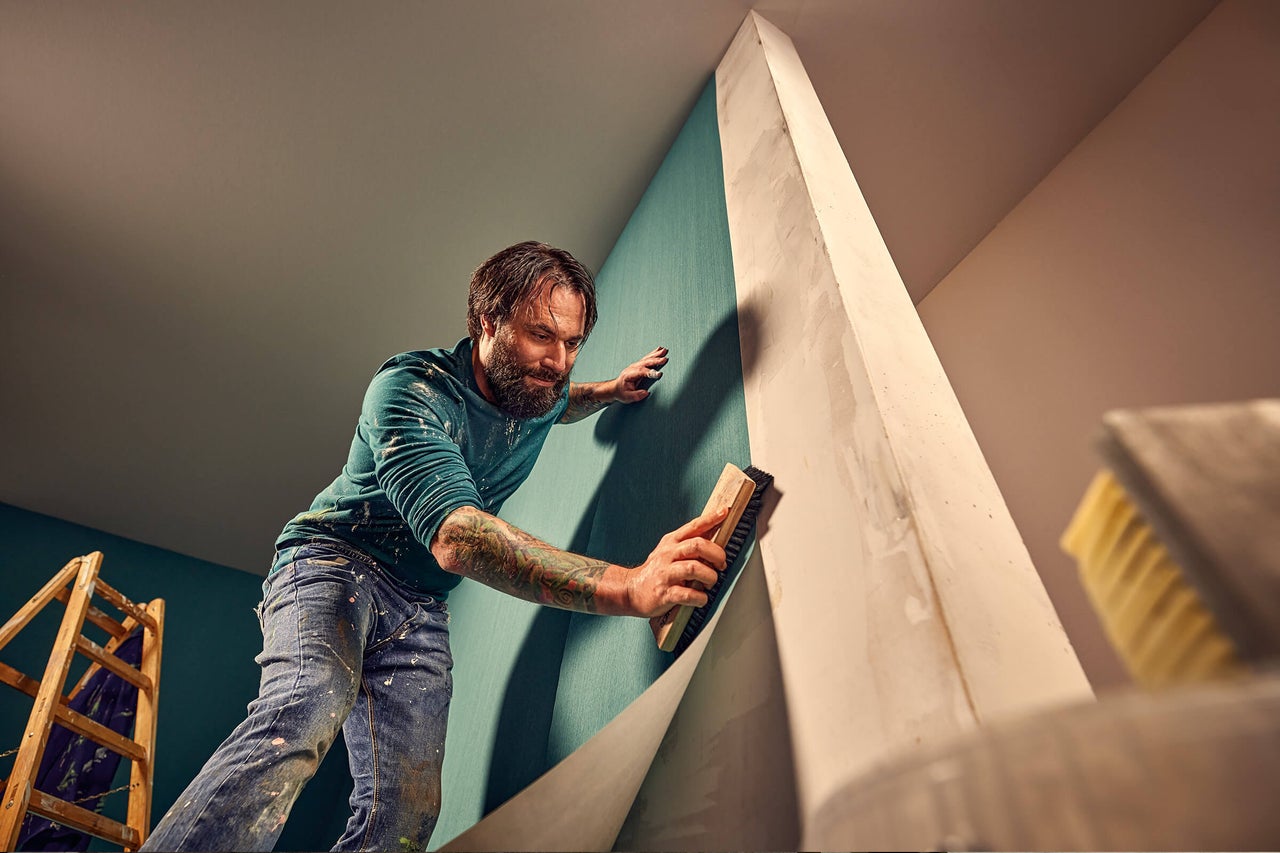 En man tapetserar en vägg med en borste. Renovering och rumsdesign är synliga.