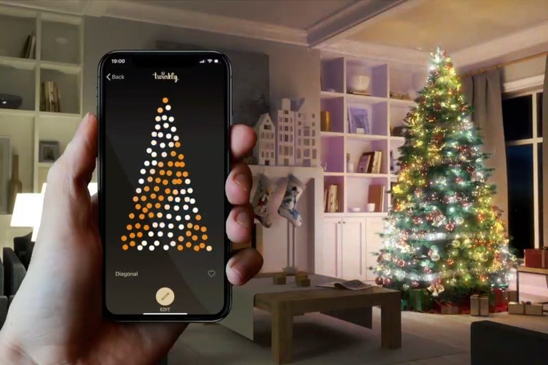 Mobiltelefon med Twinkly-app för att styra en ljusslinga på en julgran i vardagsrummet