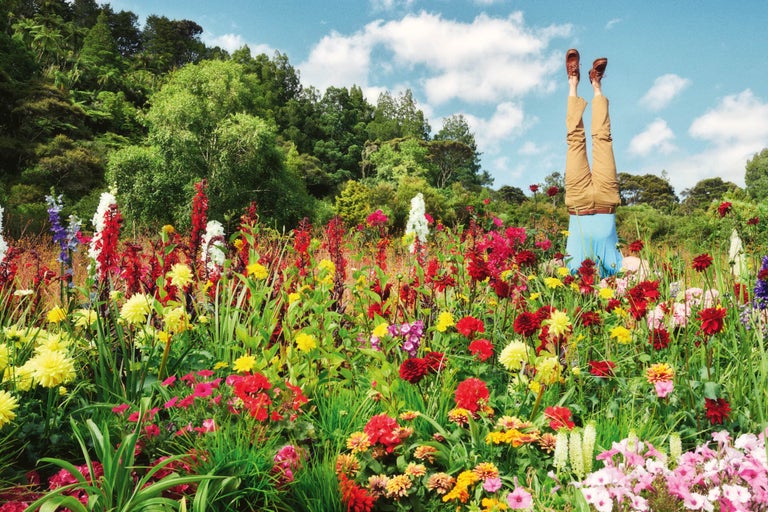 Person står på huvudet i en blommande blomsterträdgård med träd i bakgrunden