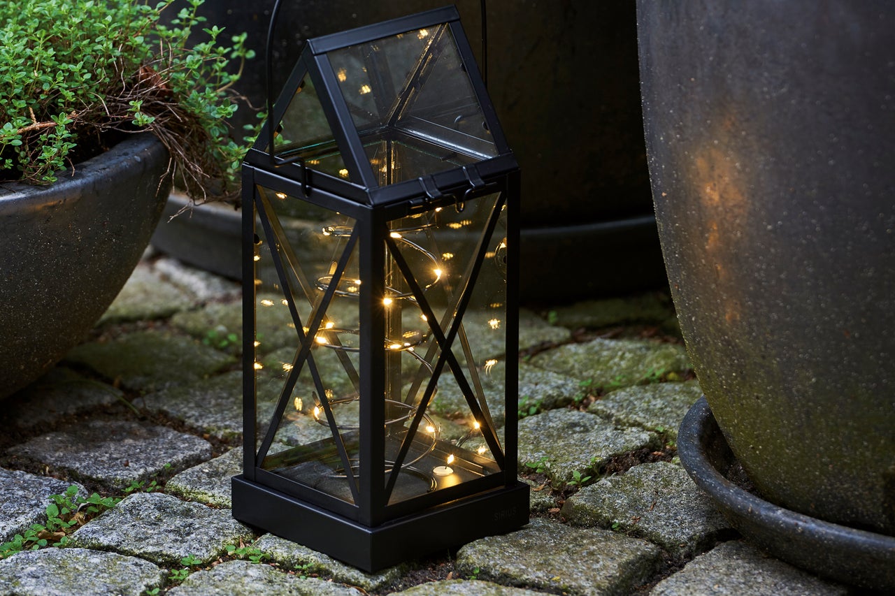 Dekorativ trädgårdslampa med ljusslinga bredvid blomkrukor på gatsten