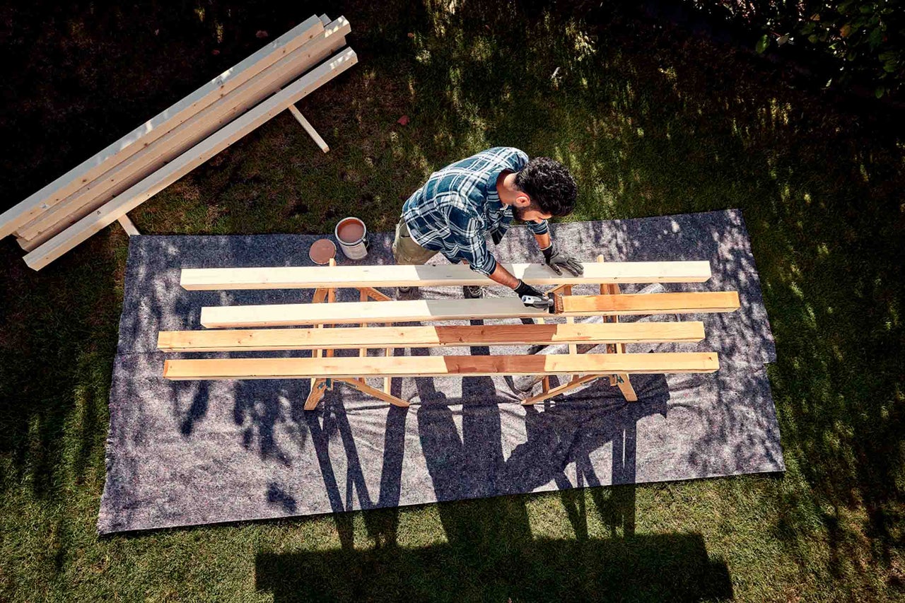 Man målar träbrädor i trädgården med träskyddslasyr på en arbetsbänk
