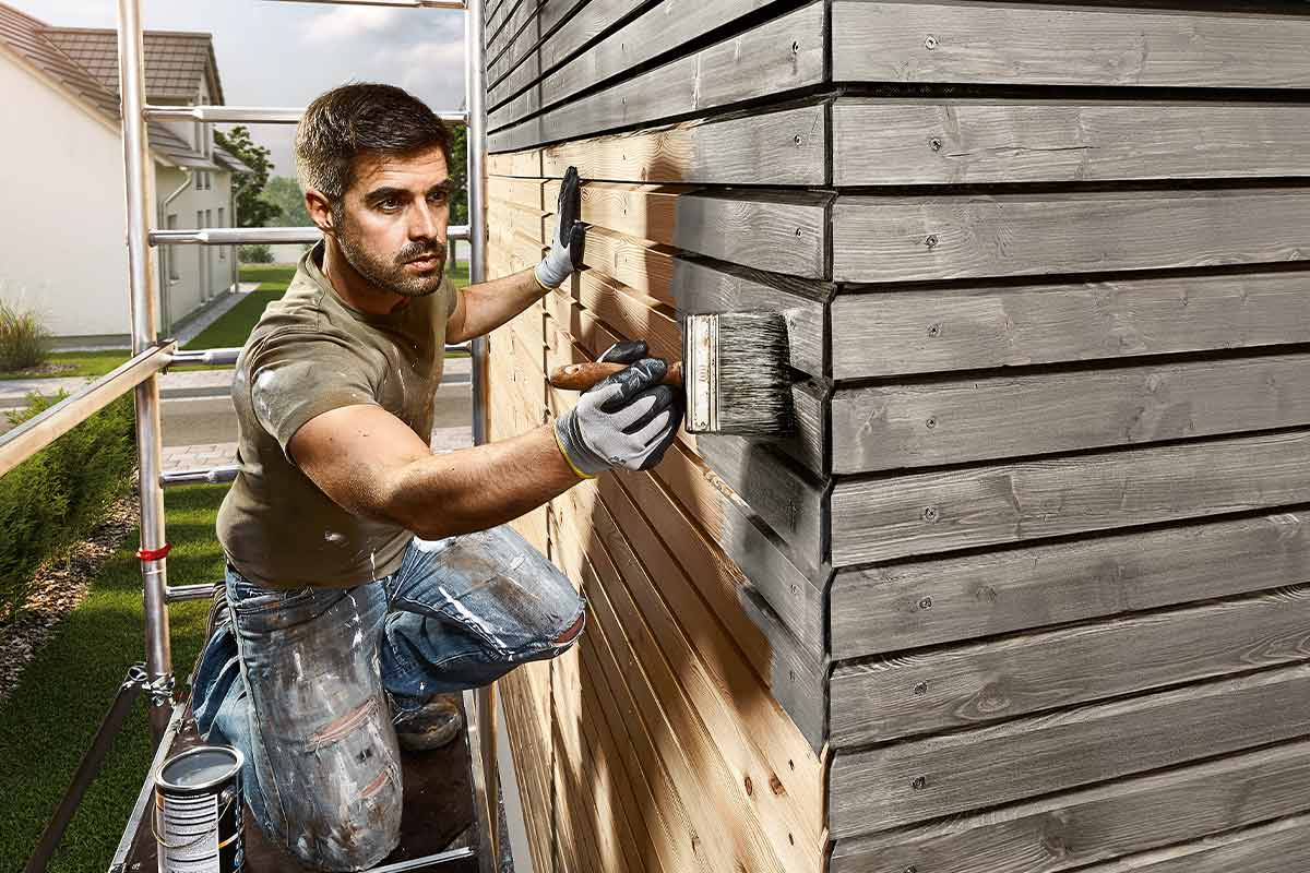 Man målar en träfasad med en pensel.