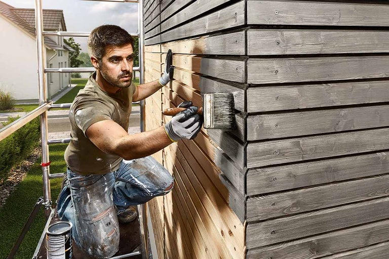Man målar en träfasad med en pensel.