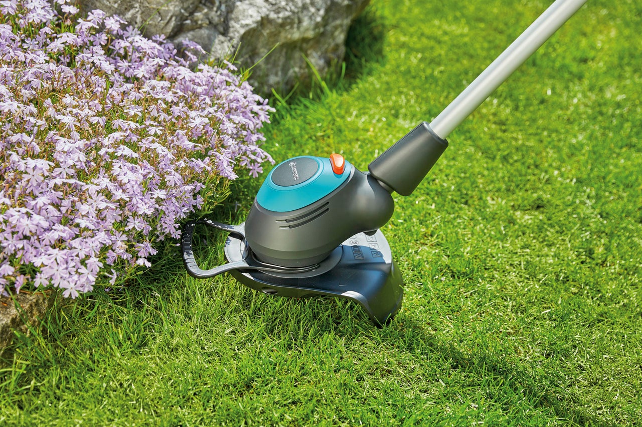 Grästrimmer i drift bredvid en blomsterrabatt i trädgården.