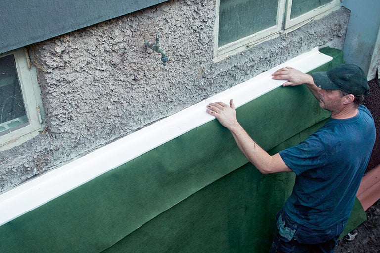 En man installerar fasadbeklädnad på en yttervägg.