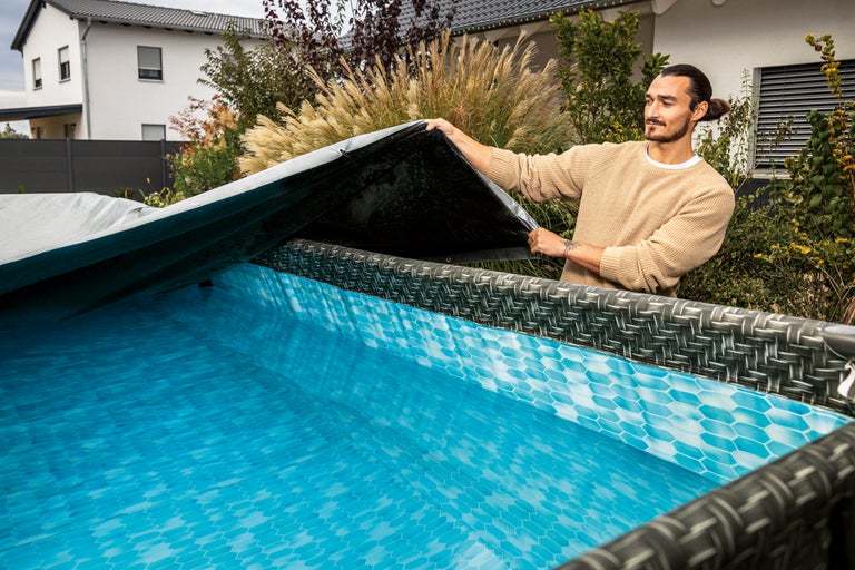 Man öppnar ett poolskydd för en ovanjordspool i trädgården.