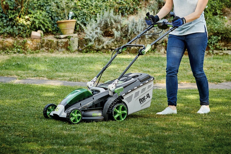 Person använder en gräsklippare av märket for_q på en gräsmatta.