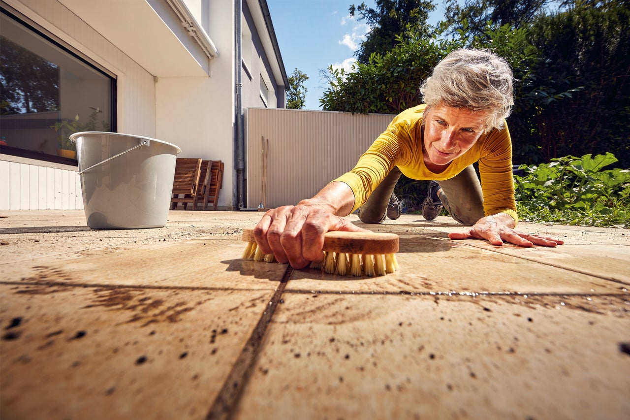 Kvinna rengör terrass med borste och hink