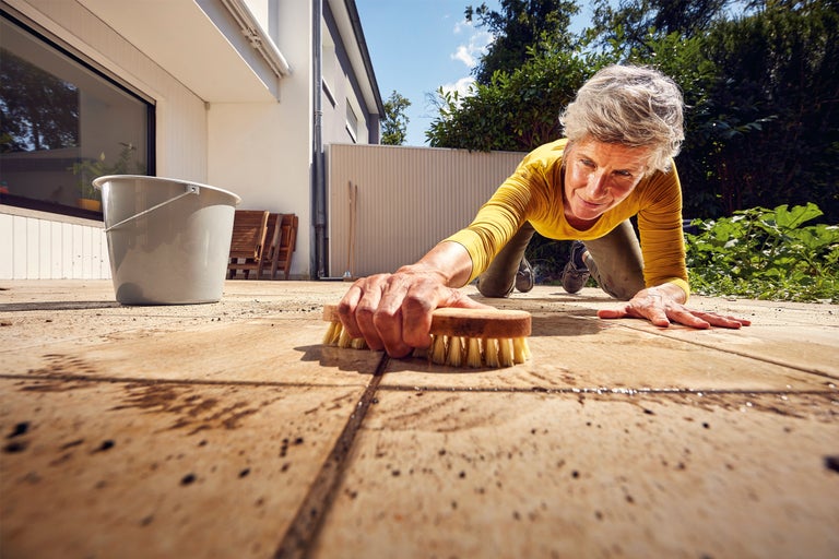 Kvinna rengör terrass med borste och hink