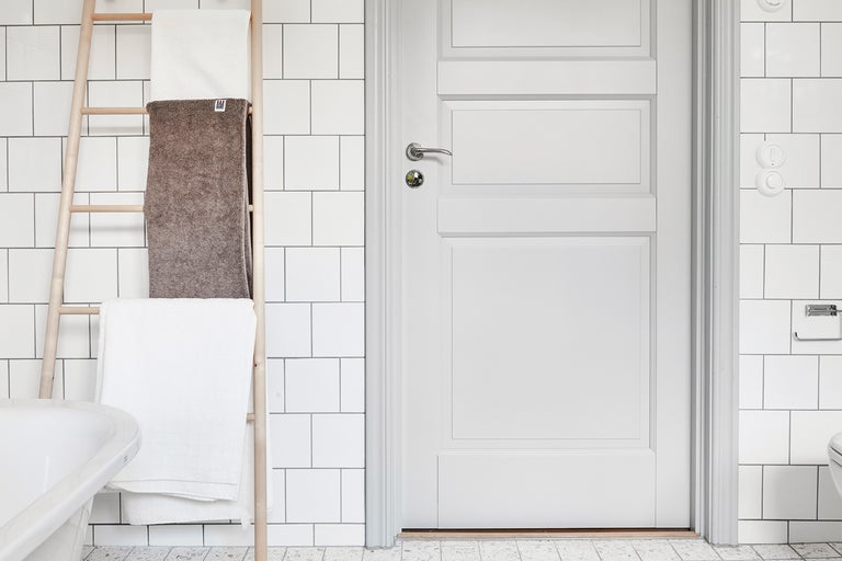 Badrum med handdukstege, vita handdukar och vit dörr