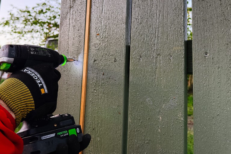 Hantverkare fäster en trälist på ett trädgårdsstaket med en sladdlös skruvdragare