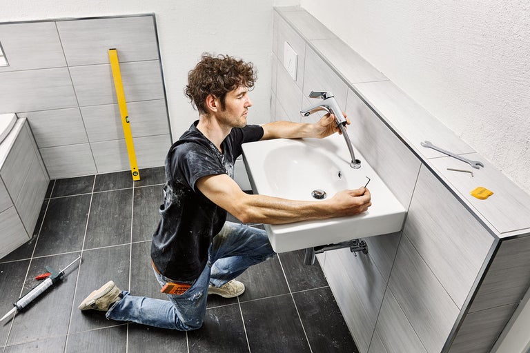 En man installerar en kran på ett handfat i badrummet.