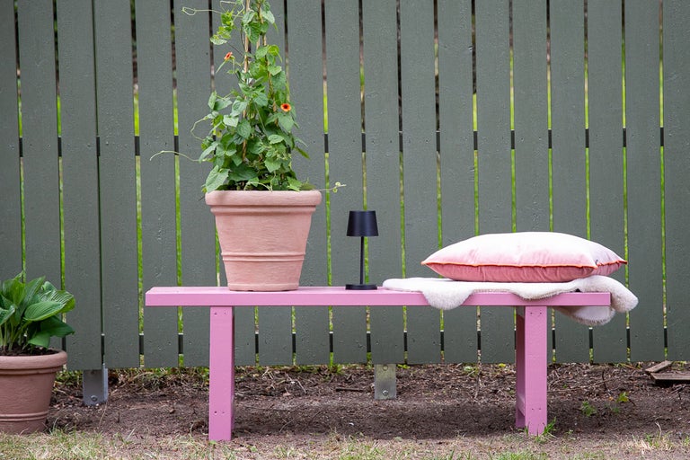 Trädgårdsscen med bänk, krukväxt, kudde och lampa framför trästaket