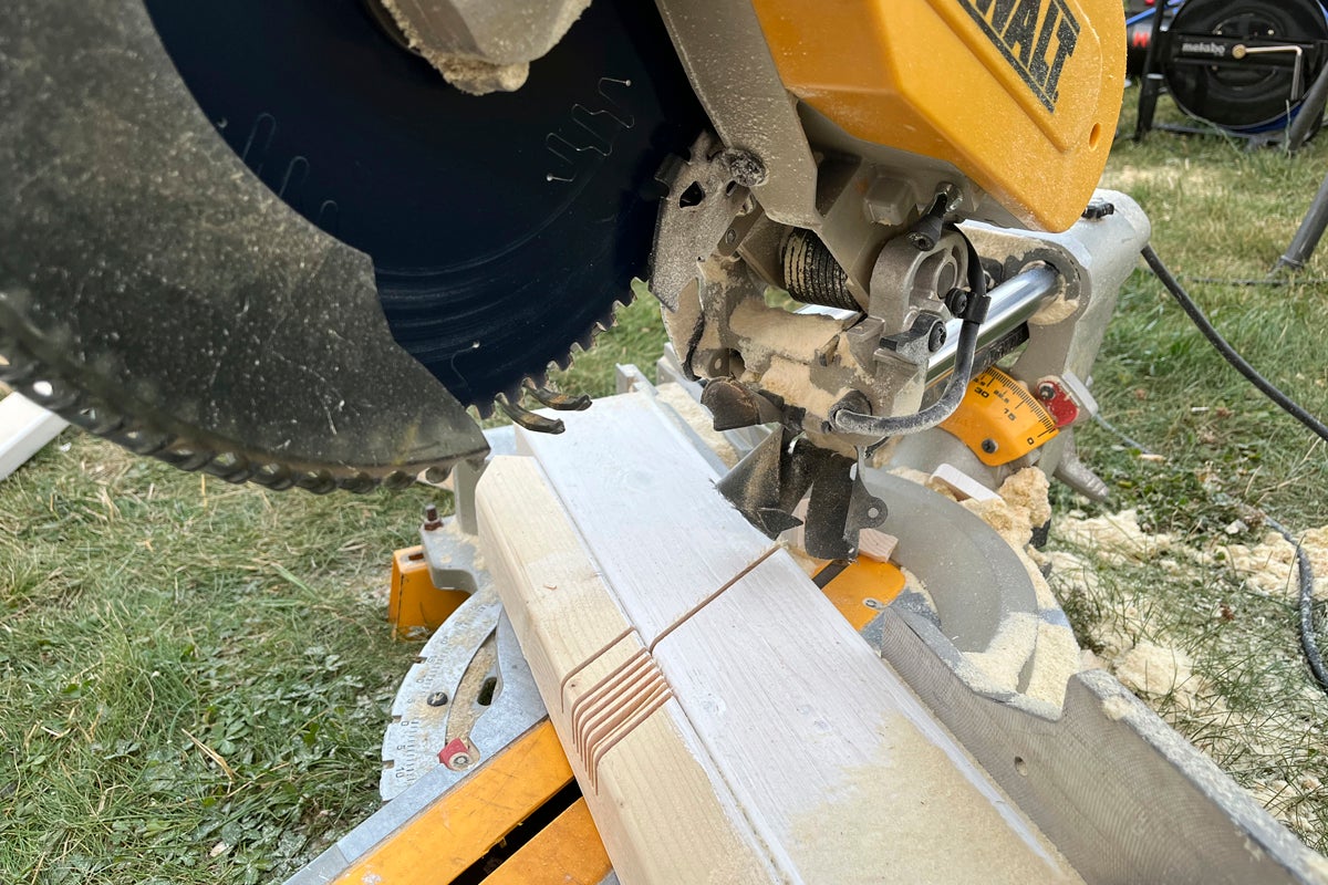 Kap- och gersåg som sågar en träbalk utomhus, sågspån på maskinen och träet, DeWalt Logo.