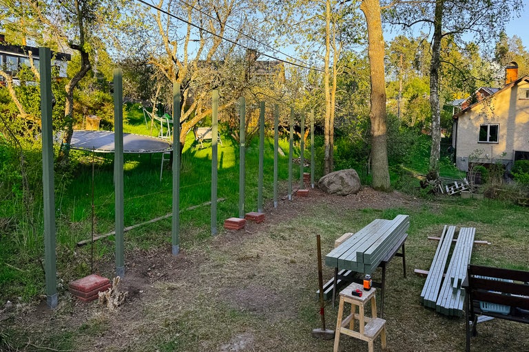 Byggande av ett trästaket i en trädgård med trästolpar och verktyg