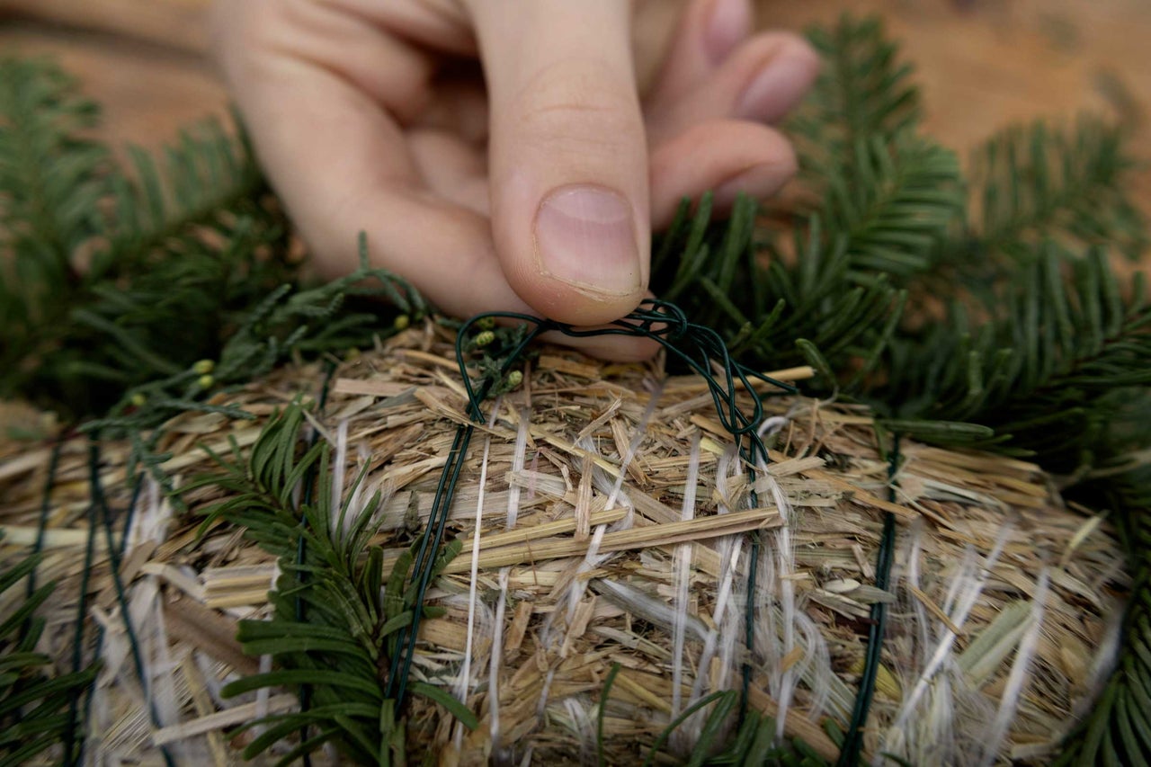 Dekorativ halmkrans dekoreras med grangrenar och bindtråd.