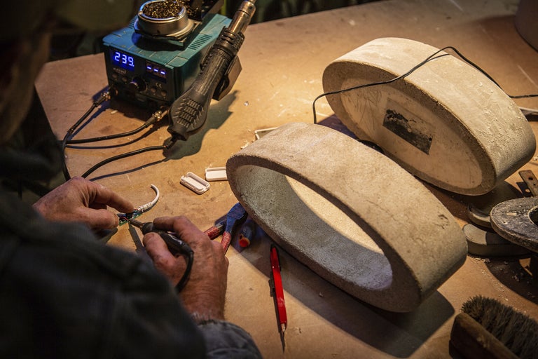 En person löder en kabel på en arbetsbänk med slipstenar och lödkolvar.