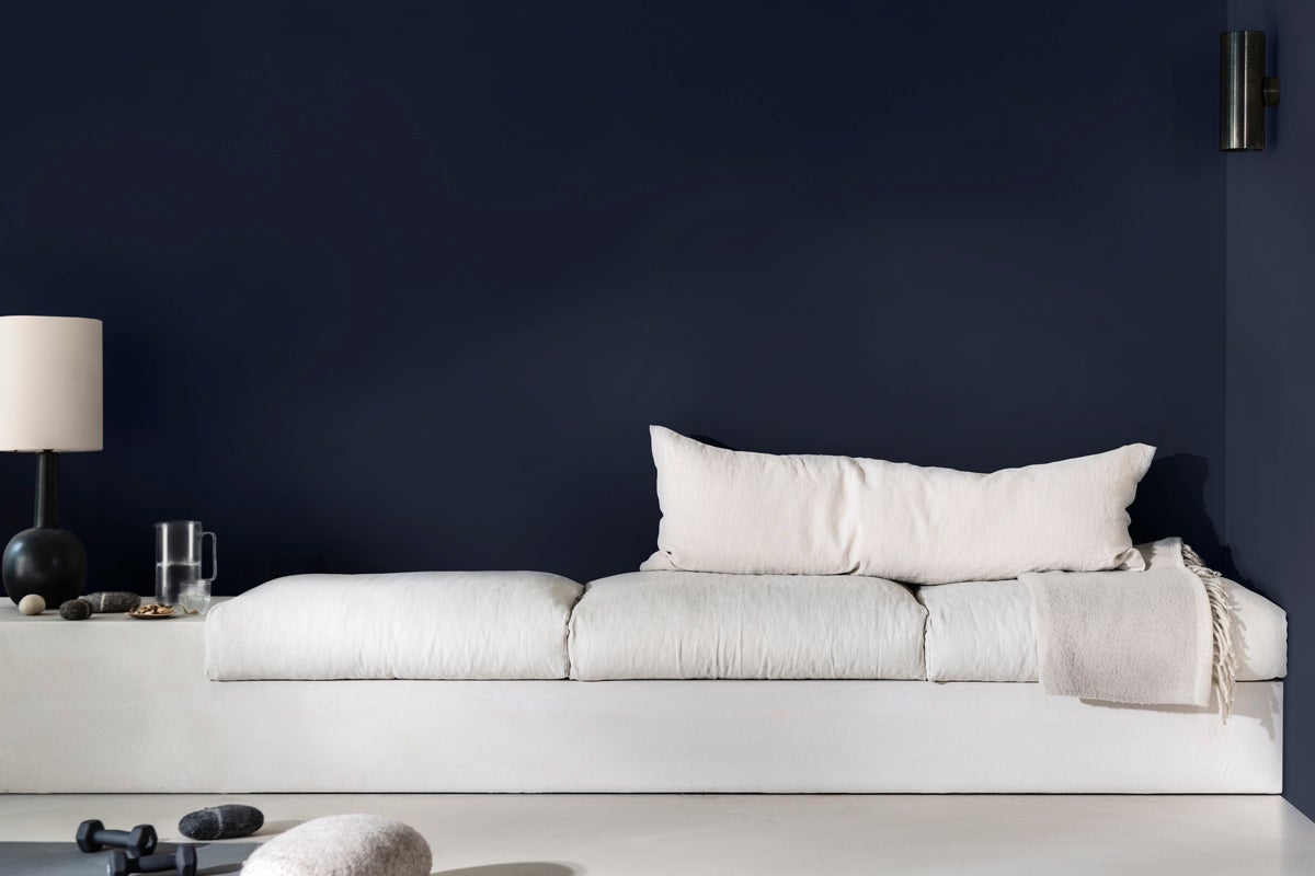 Modernt vardagsrum med soffa, lampa och dekorativa föremål framför en mörk vägg