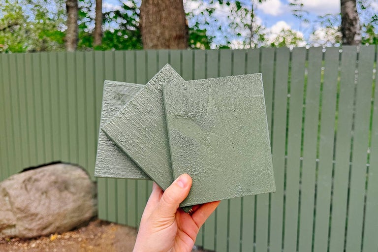 Tre färgprover av trä för utomhusbruk hålls framför ett trästaket
