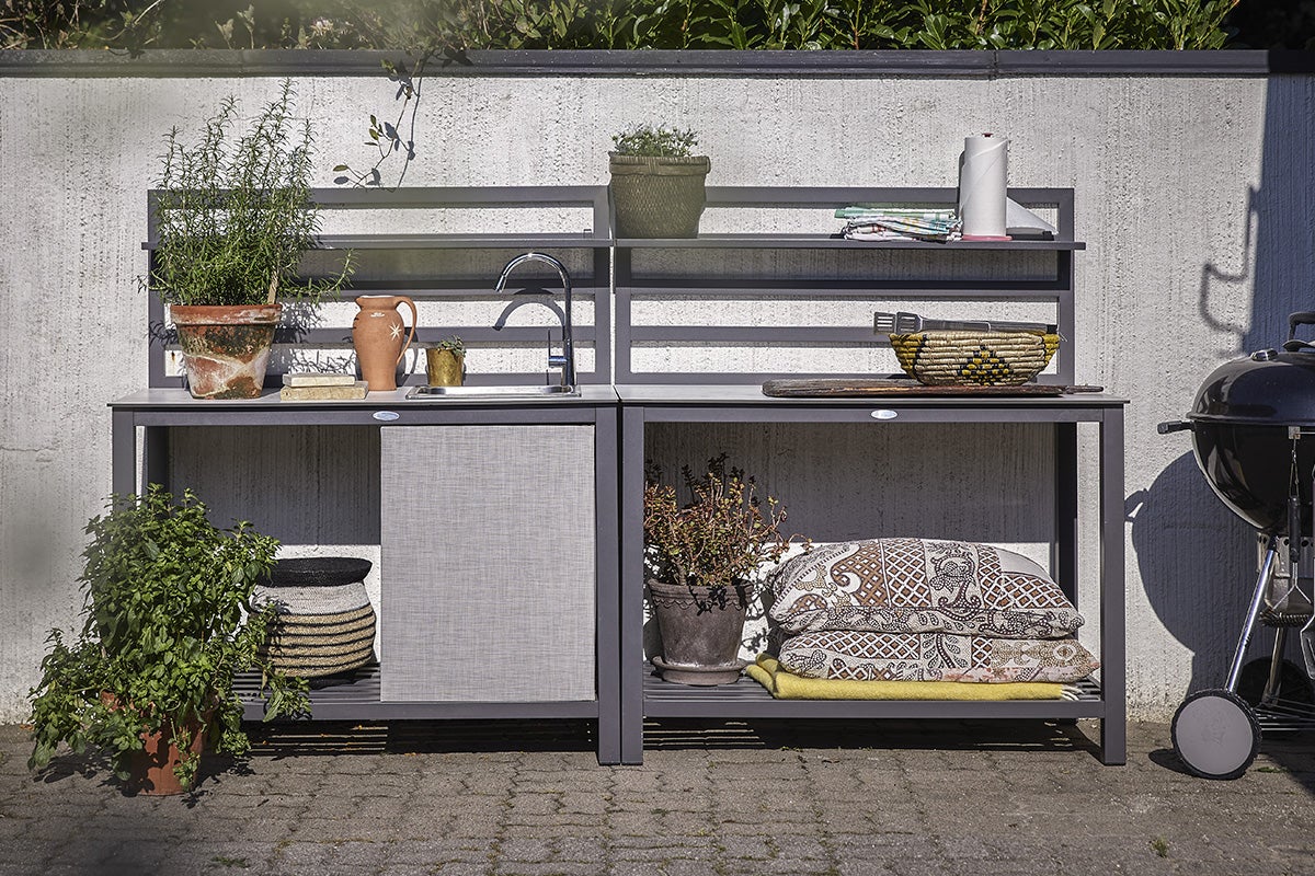 Utomhuskök med hyllor, diskho och grill bredvid mur