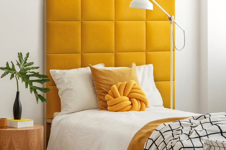 Sovrum med vadderad sänggavel, kuddar och sängbord med dekoration