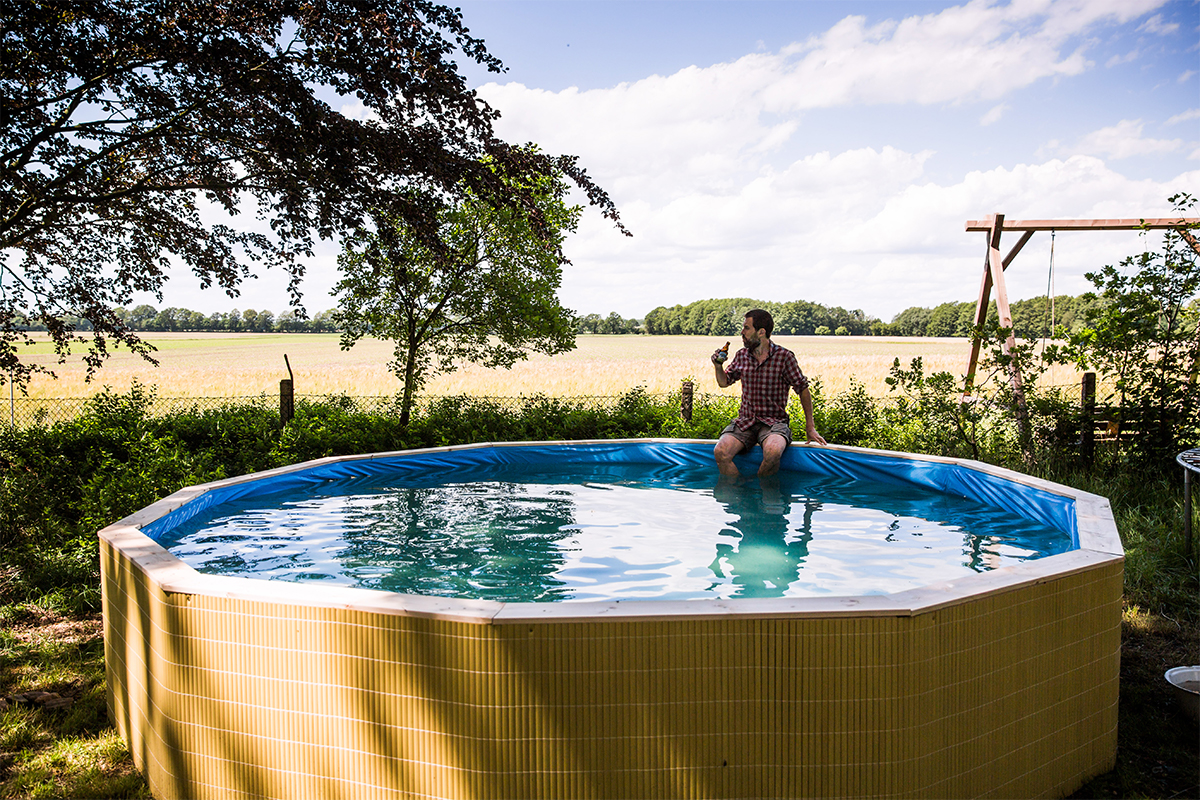 Ovanjordisk pool i trädgården med en person som sitter på kanten och njuter av en drink