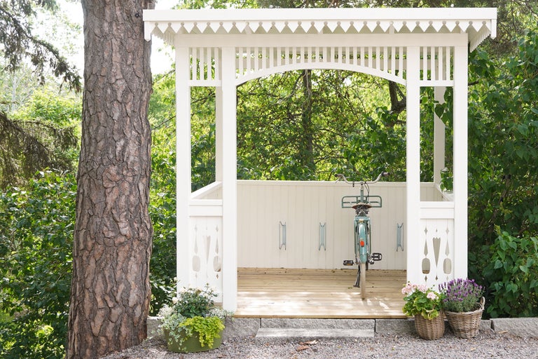 Vit paviljong med cykelställ och cykel framför träd