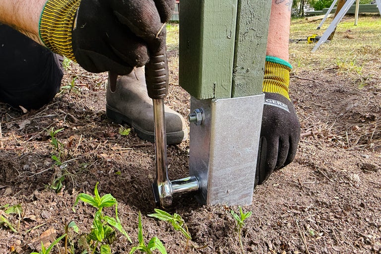 Personen fäster en stolpe med en metallstolpsko i trädgården.