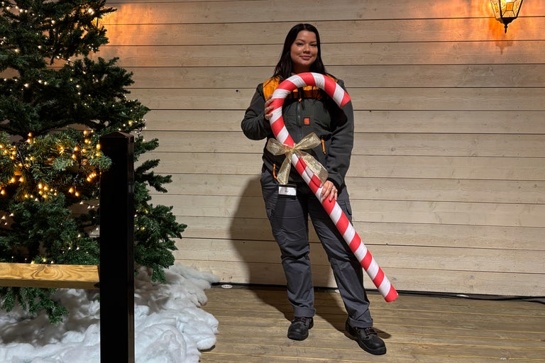 En kvinna håller en stor polkagrisstång framför en julgran