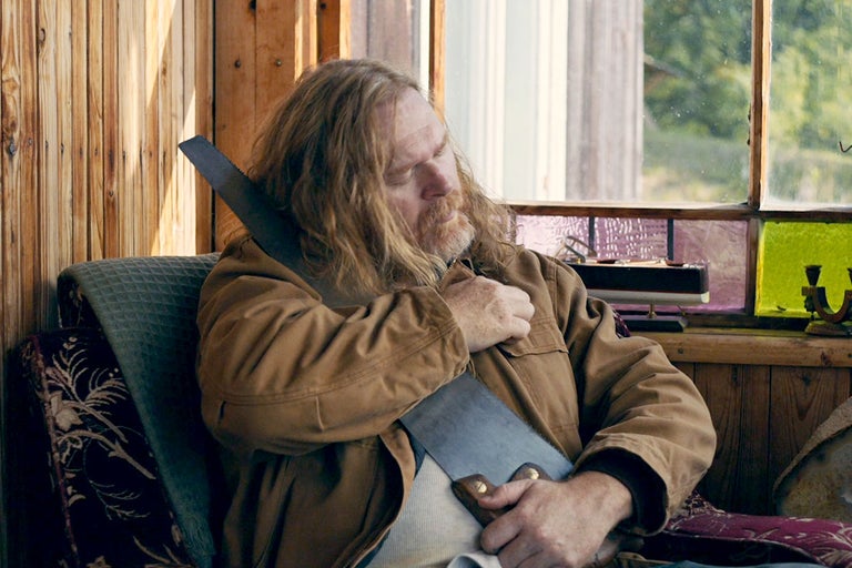 En man sitter på en stol med en handsåg