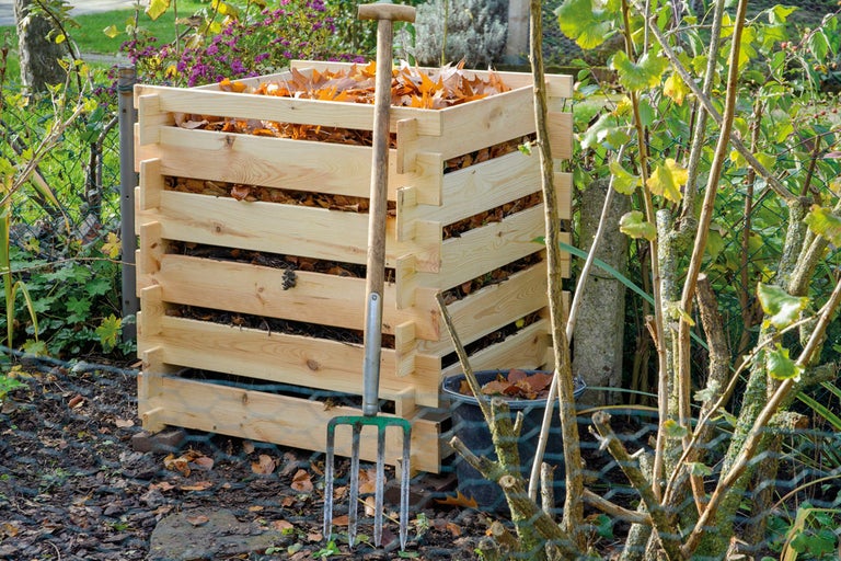 Träkompost med löv och en grep i trädgården.