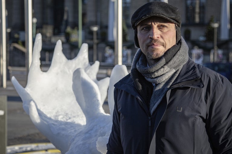 Man med halsduk och mössa framför snöskulptur