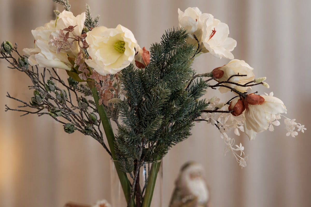Konstgjort blomsterarrangemang med amaryllis och tallkvistar i en glasvas som juldekoration.