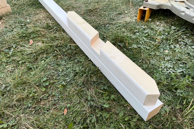 Vitmålad staketstolpe av trä med urtag för montering på en gräsmatta.