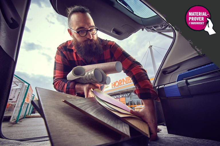 Man lastar bagageutrymme med laminat, tapeter och färgprover framför en Hornbach-butik