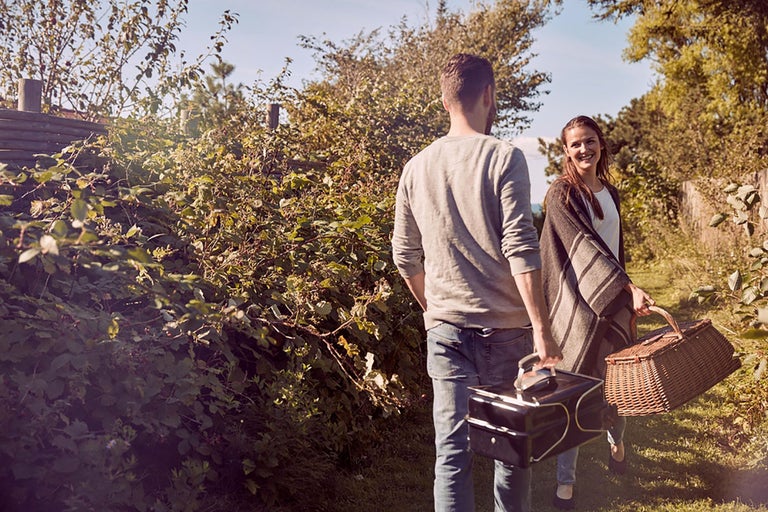 Ett par promenerar genom naturen med en picknickkorg och en grill.