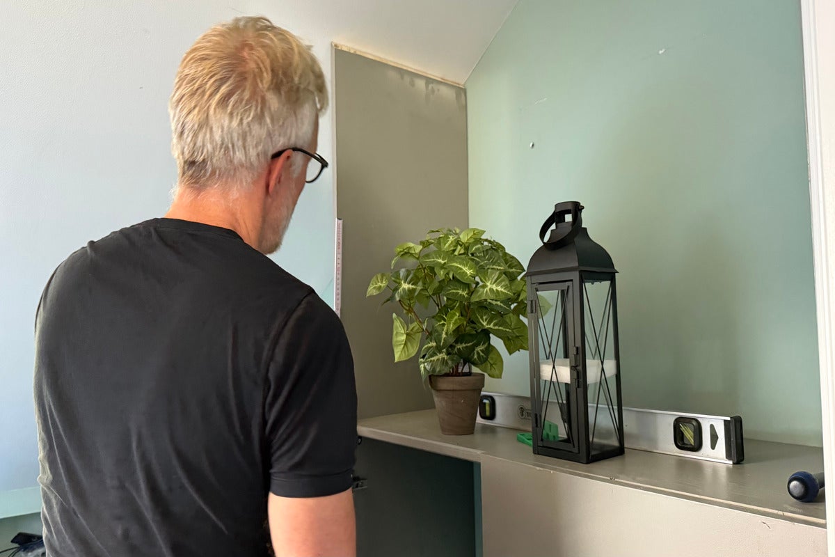 Man inreder rum med växt, lykta och vattenpass på en hylla