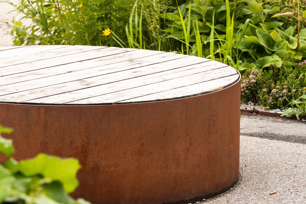 Rund trädgårdsbänk med träyta och rostfärgad metallbas