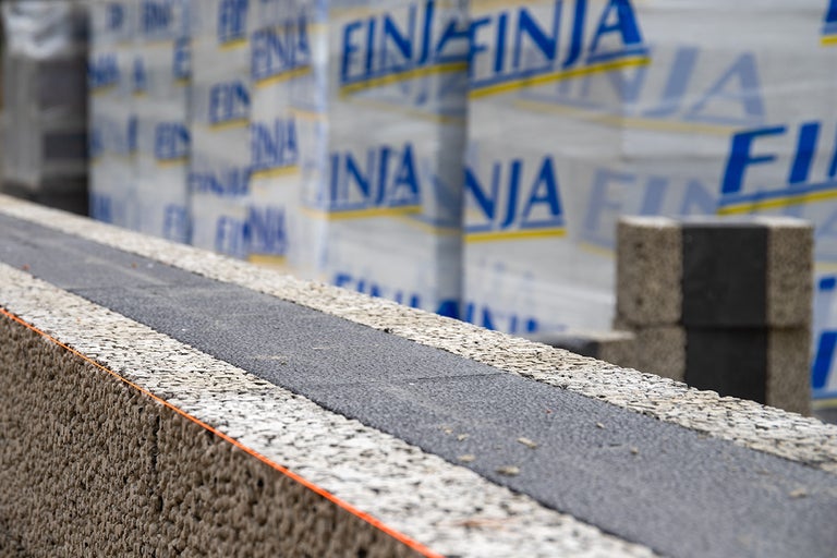 Vägg av lättbetongblock med isoleringsremsor och pallar med FINJA-stenar i bakgrunden